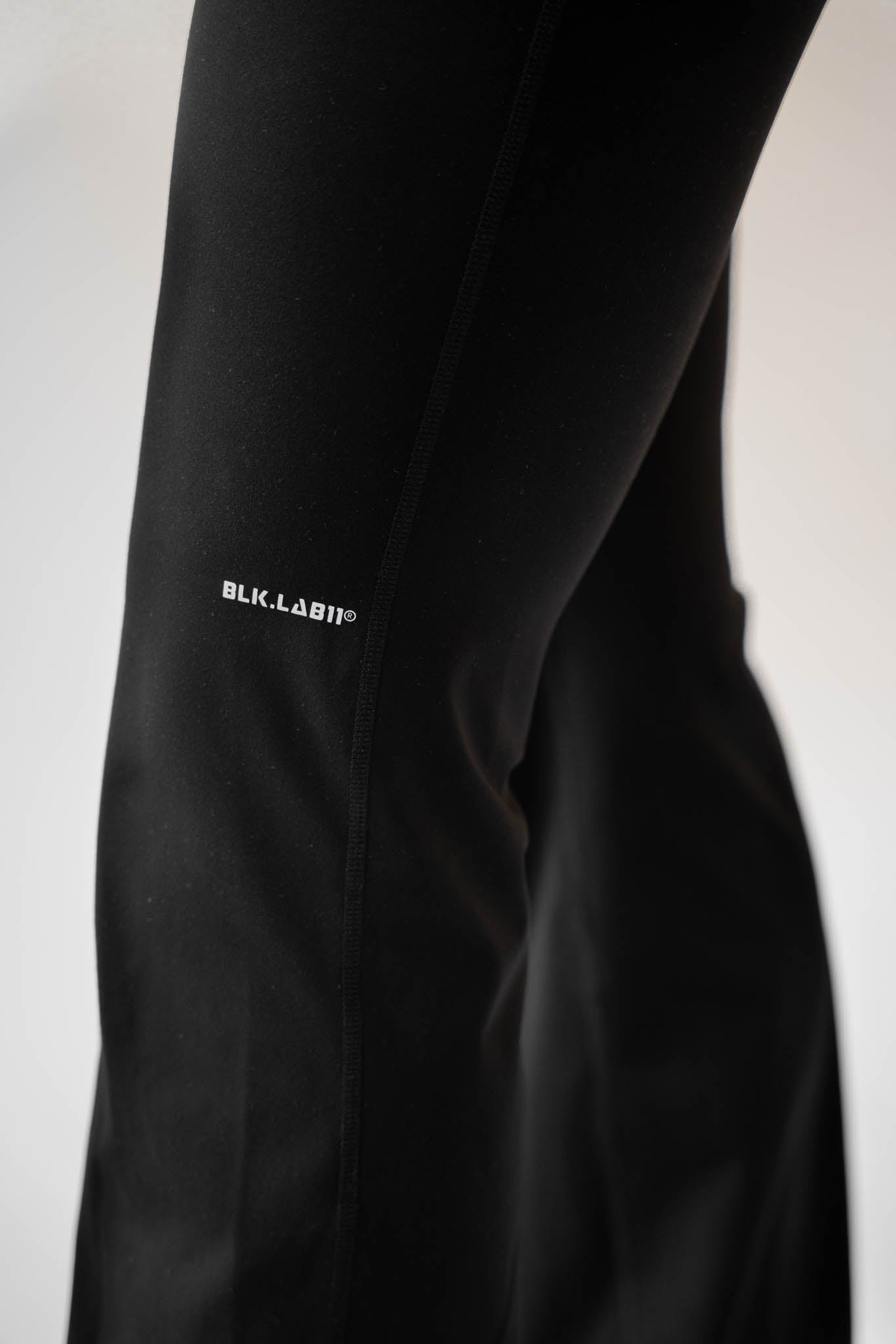 Detalje af sorte flare pants med BLK.LAB11 logo på benet.